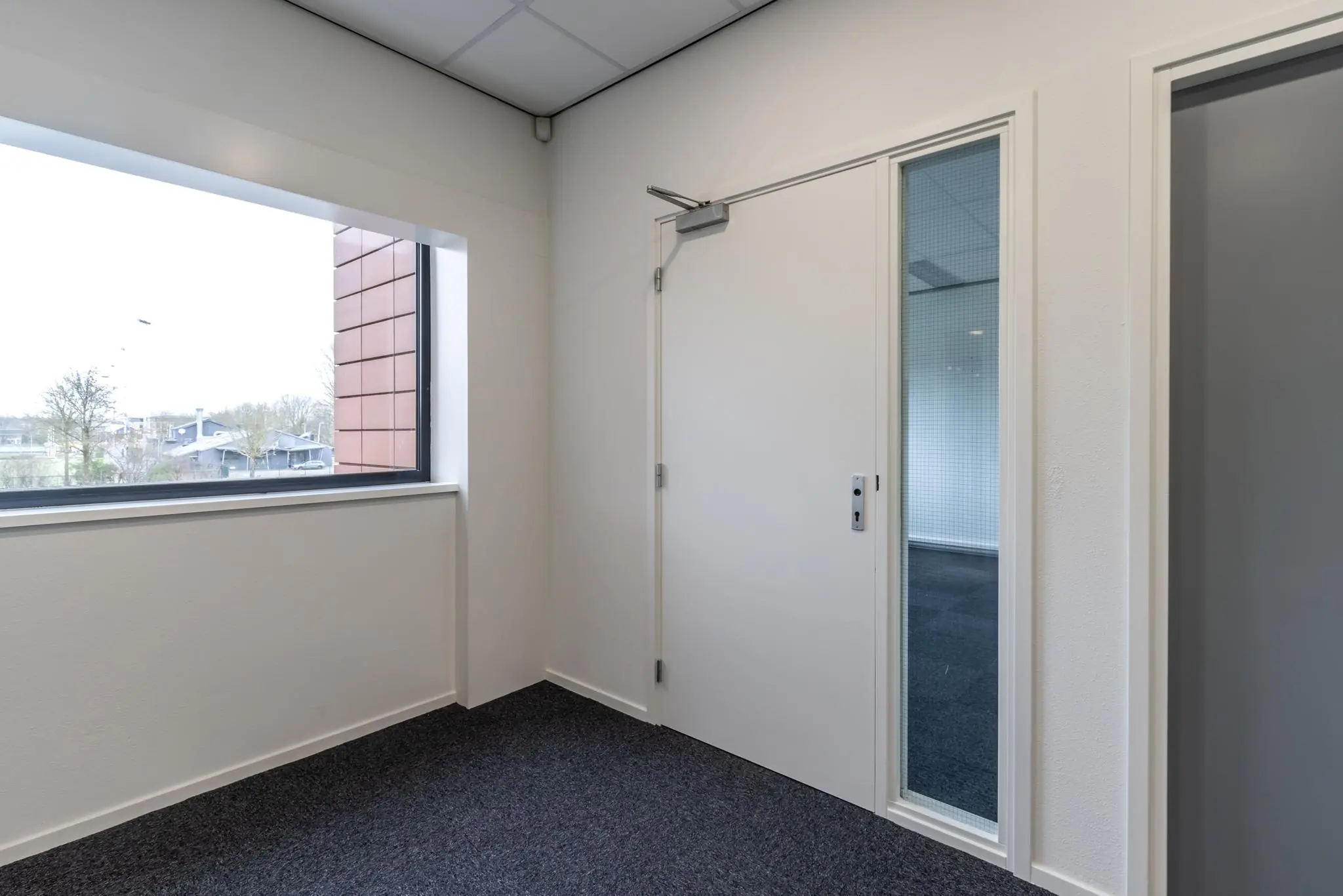 Kleine kantoorruimte aan de Lage Biezenweg met raam, deur en zicht op naastgelegen kamer.